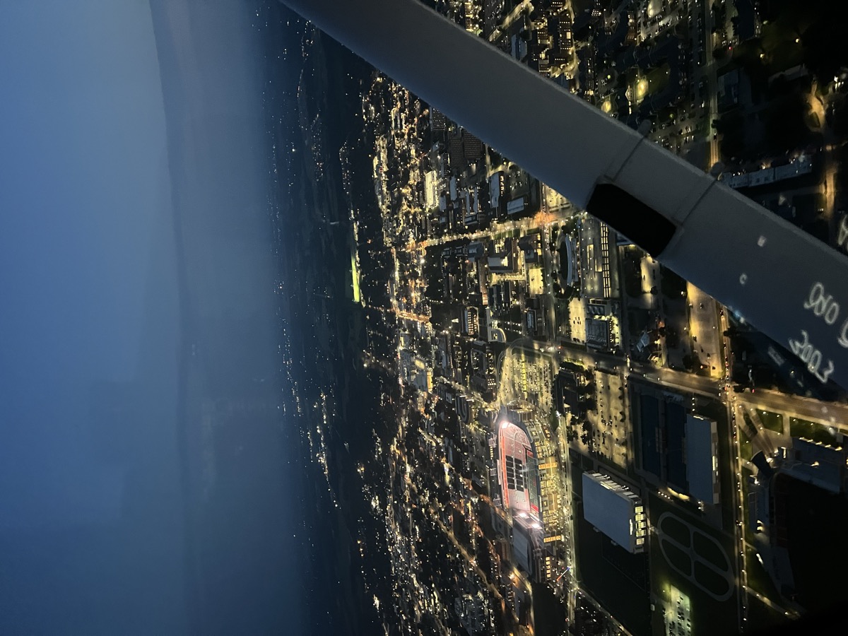 City lights at night seen from the cockpit over the wing strut