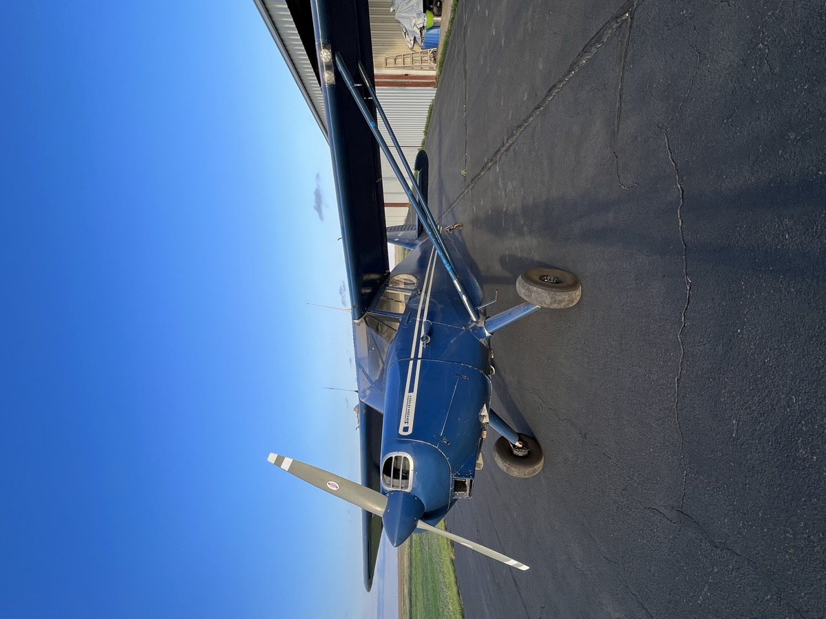 Blue Stinson taildragger parked on the ramp by a hangar