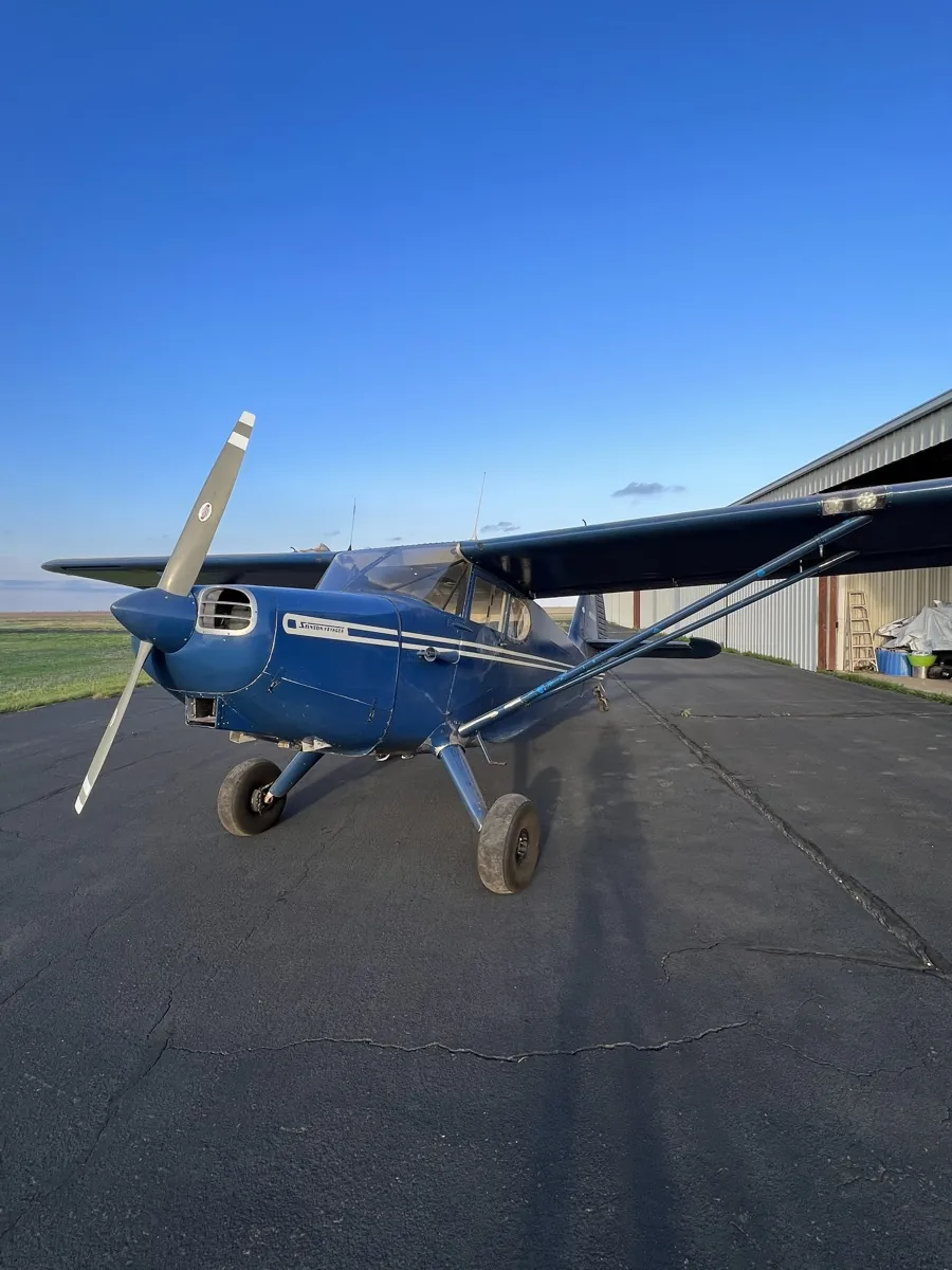 Blue Stinson taildragger parked on the ramp by a hangar